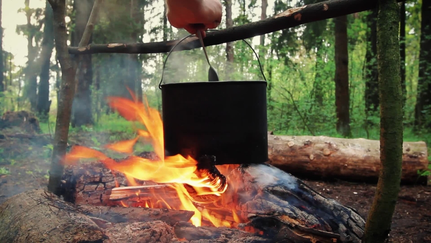 Preparing of cooking in woods outdoor. Cook soup or porridge with meat in hiking trip. Tourist warms up dinner in campfire. Camp on travel, place for bonfire. Survival in wild adventure in summer | Shutterstock HD Video #1054341287