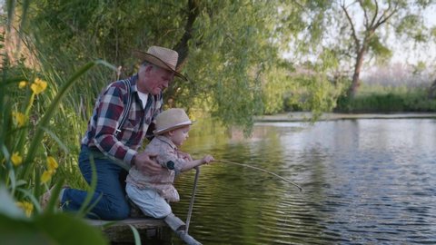 family vacations, elderly caring grandfather with his attractive little grandson have fun playing on pier by river while relaxing in countryside