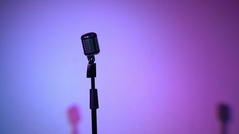 Professional concert vintage silver microphone for record or speak to audience on stage in dark empty retro club close up. Spotlights shine on a chrome mic on multi color background.