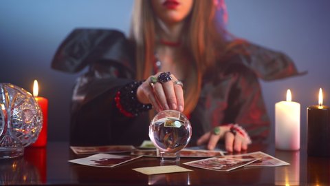 Mysterious gypsy with red lips spelling over people pictures and moving hand abovemagic crystal ball. Witch talking with spirits and afterlife, black potion and bad prediction