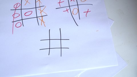 View of the hands of dad and a small child. Dad plays tic tac toe with his daughter on a sheet of paper.