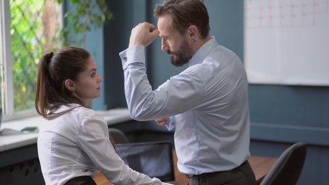 Rear view. Business man showing off to employee female the strength of his muscles forcing her to touch his hand. Harassment concept. Psychological state concept. Business concept. Prores 422.