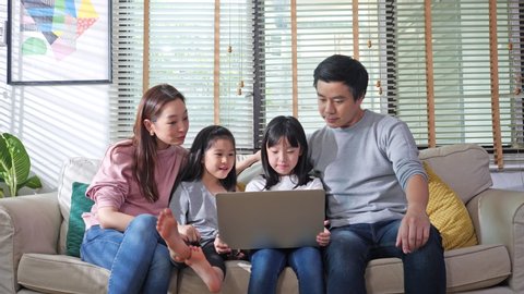 Authentic close up of asian family watch TV show online on laptop in living room at home. Father, mother and children enjoyment with conference online in internet while being quarantine at home.