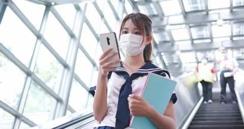 Asian girl high school student take escalator in the mrt station with facial mask and use mobile phone