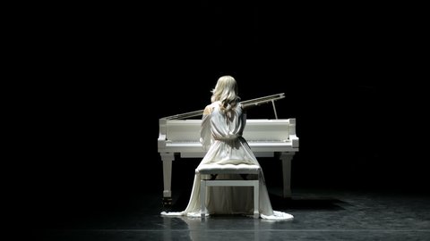 Pianist plays beautiful white grand piano on stage in concert . View from the back.