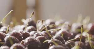 On a berry background of wet cherries with droplets of water a female hand puts a ripe cherry. Splashes of water on a cherries background. Slow motion video in 4k. Shallow depth of field.