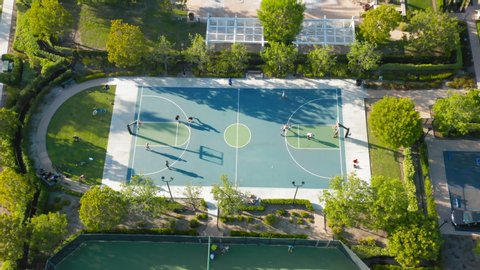 4K aerial bird-eye view of a basketball court. Basketball game on the sport field in a green park area in the sunset light. Two basketball sports teams actively play with a sports ball.