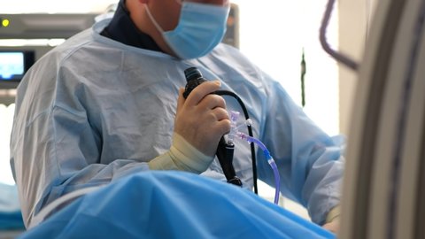 A doctor in a dressing gown, mask and rubber gloves performs a stone crushing operation in the operating room. Endoscopic surgery on the monitor. 