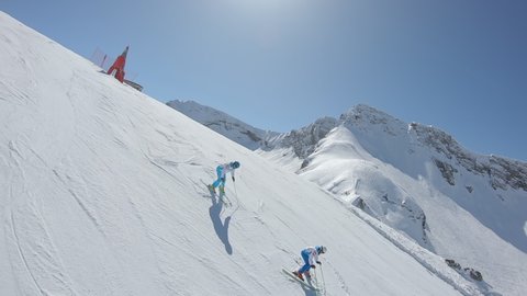 FPV drone AERIAL: a group of professional skiers ride synchronously along the track in white and blue suits. four ski instructors demonstrate synchronized slalom. Drone for racing, action movies, 2k
