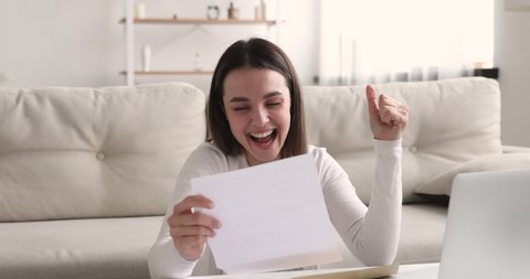 Curious young 20s girl opening envelope with correspondence, reading paper letter, excited by good news. Overjoyed happy female student received university admission notification or grant payment.