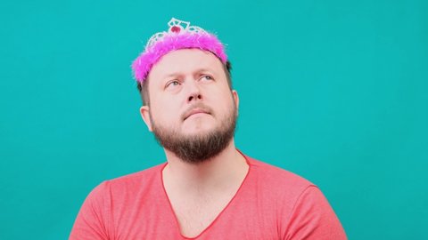 funny bearded freaky man in a pink T-shirt with a deadema on his head is dreaming with a magic wand in his hand. A funny wizard joke to make and fulfill a wish