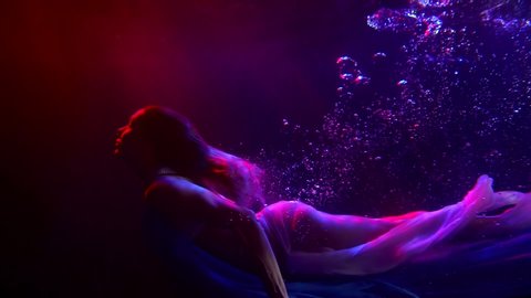 half-naked woman is swimming in depth of big pool in neon lights