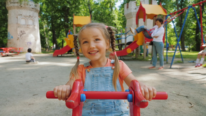 Cute pretty child rides on balancing swing. Little girl laughing and having fun, swinging on seesaw board, playing playground. Concept of happy childhood, positive emotions, POV | Shutterstock HD Video #1054363799