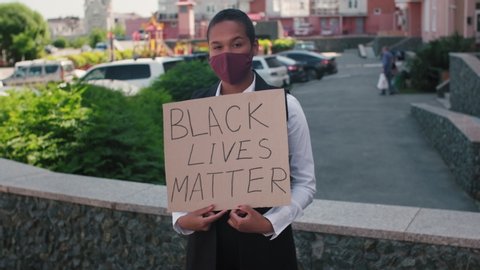 Tracking portrait of young African-American woman standing outdoors and holding sign Black Lives Matter
