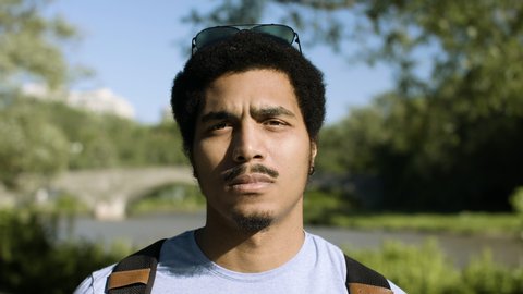 A portrait of a handsome black man looking confident in a beautiful park with a river in the background. Shot in 4k. 