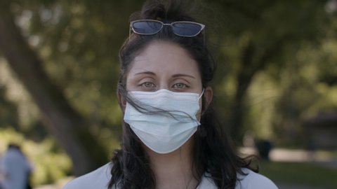Authentic portrait of a young woman wearing a medical mask in a beautiful public park. Shot in 4k 