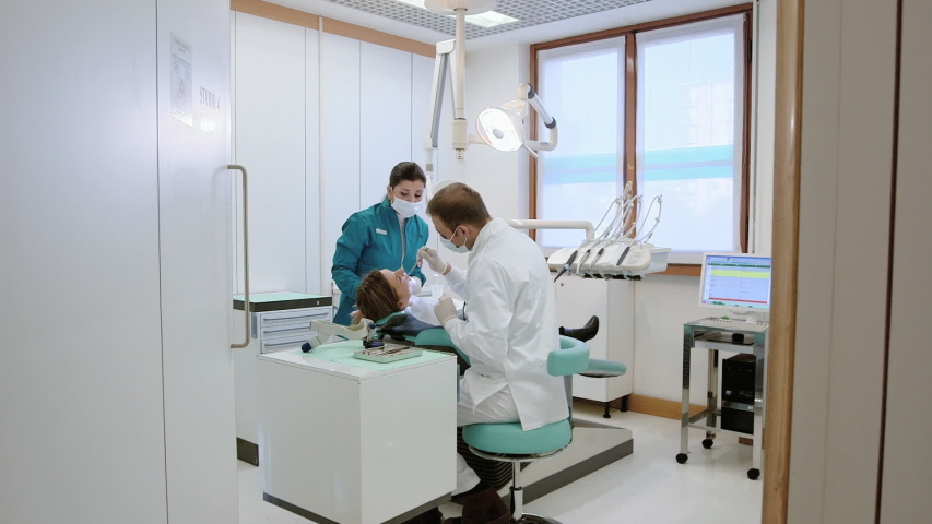 People health and dental care, man at work as dentist with assistant and visiting young woman as client in professional lab of medical clinic. Steadicam shot | Shutterstock HD Video #1054366799
