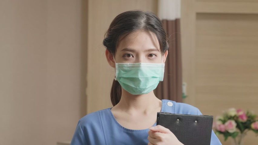 Portrait shot of Female medical nurse in medic uniform taking surgical mask off face, looking at camera and smile in slow motion shot. Beautiful Asian young woman worker is smiling in hospital. Royalty-Free Stock Footage #1054367558