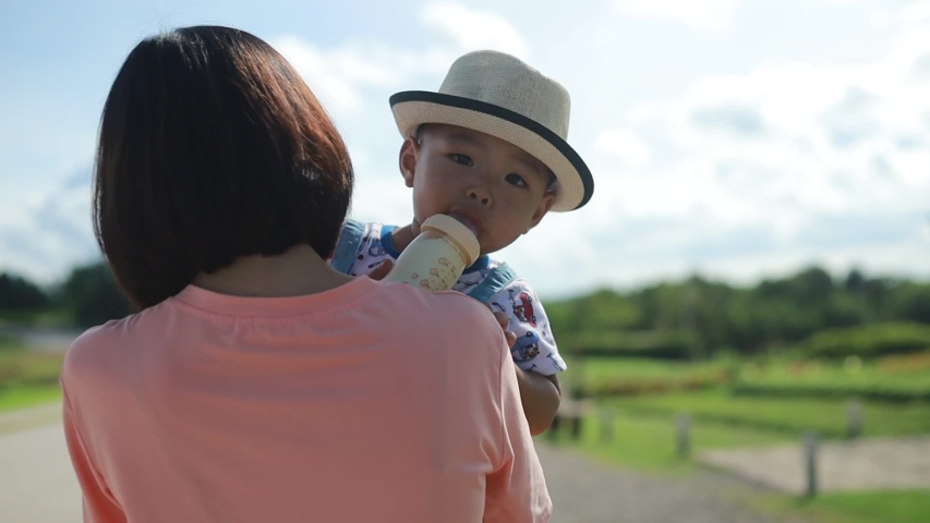 Slow motion of back of the Asian mother walking and carrying her son.