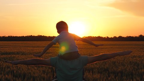 Father holding son on shoulders, imitating the flight of the aircraft. Silhouette of a happy family at sunset. The concept of generations, education of children, freedom.