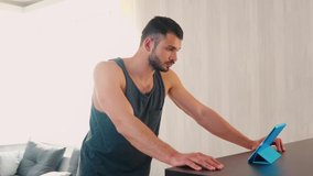 Young man exercising at home. Fintess trainer explain during video call on tablet and to raise up dumbbells up and work with chest muscles. Help non professional sportsman online.