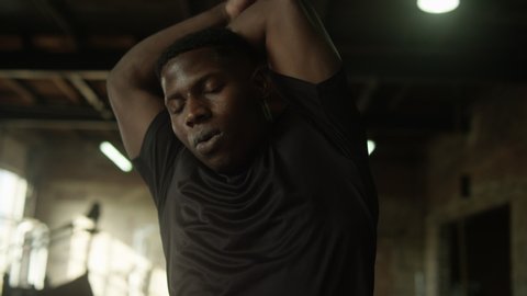 Young, fit African American man stretching his shoulders in industrial-style gym