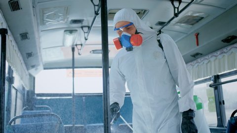 Man disinfect bus covid-19 mers. Corona virus flu disinfection. Coronavirus disinfectant indoors. Worker wear white uniform inside. Protect mask. Spray disinfecter. Danger work. Respiratory face mask.