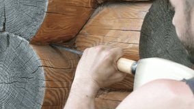 Close-up of a man caulking a log cabin. A carpenter is building a wooden house. Work in the countryside. UHD video.