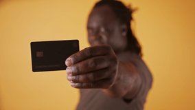 Happy african man in white showing credit card at camera over orange background.