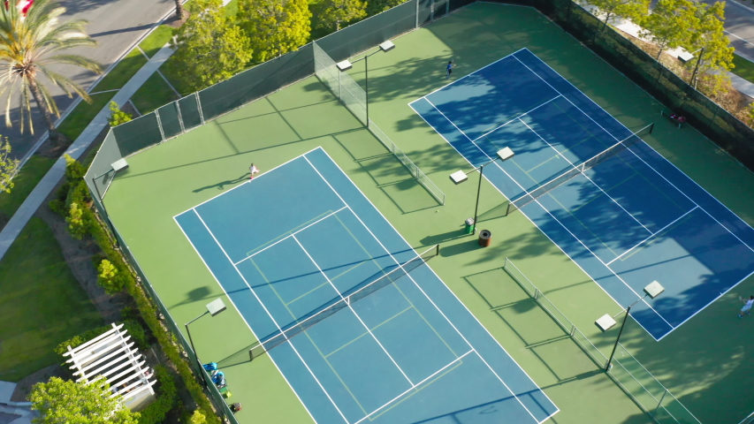 4K drone camera moves around a tennis court where there is an active game match. High quality 4k drone footage. Tennis court in the suburban area surrounded by the lavish green at sunset time. Royalty-Free Stock Footage #1054379672
