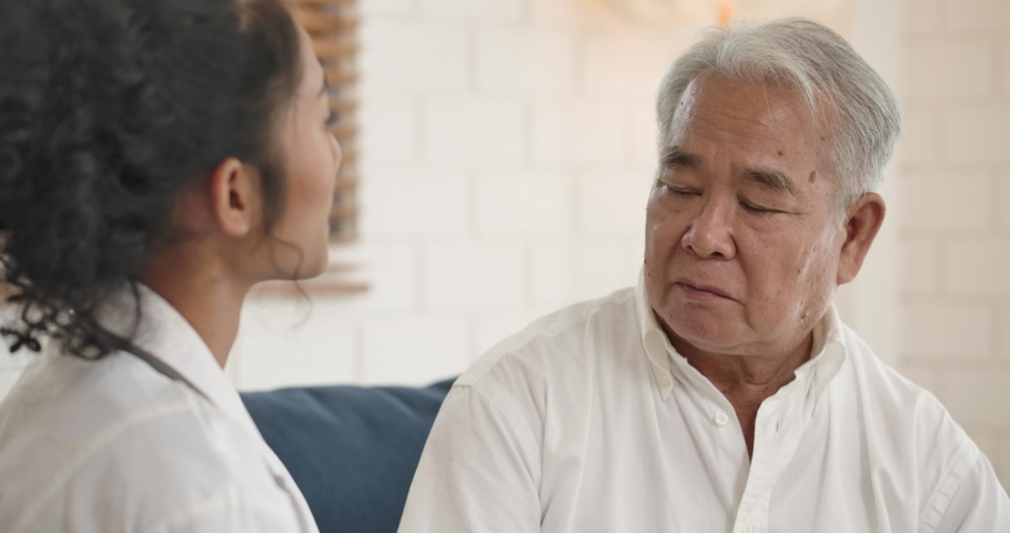 Young asian female nurse caregiver supporting talking to elderly man patient help with problem, Doctor therapist in uniform on sofa at home hospital cheering give empathy listen to senior patient. Royalty-Free Stock Footage #1054380359