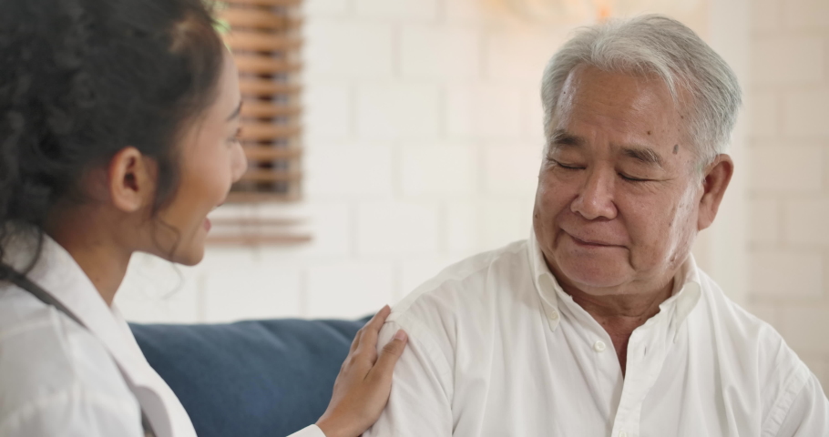 Young asian female nurse caregiver supporting talking to elderly man patient help with problem, Doctor therapist in uniform on sofa at home hospital cheering give empathy listen to senior patient. | Shutterstock HD Video #1054380359