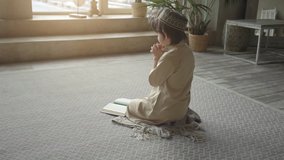 Adorable muslim child in prayer hat and arabic clothes with rosary beads and Koran book praying to Allah, prophet Muhammad holy spirit religion symbol concept inside eastern interior - Powered by Shutterstock - Get 15% off with code: PIKWIZARD15