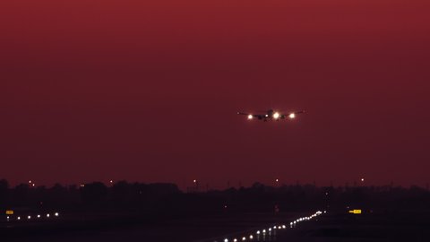 Generic Jet Airliner Night Landing on Runway with Lights-On Flying from Vibrant Red Orange Sky during Evening Airport Arrival Aviation Scene