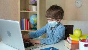 Distance education online lesson learning concept. Child Boy Kid schoolboy in protective medical mask using laptop computer for homework, studying at home. Coronavirus COVID-19 quarantine, 4 K slow-mo