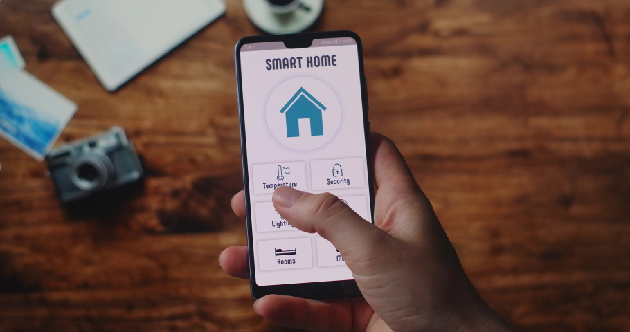 Manage smart home technologies from the office. On the background of the desktop, hands hold a smartphone with the smart home app and set the temperature and alarm in the house Royalty-Free Stock Footage #1054389251