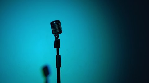 Concert vintage microphone for record or speak to audience on stage in dark empty retro club. Flashes of spotlights blink every second, changing colors. Chrome mic on multi color background.