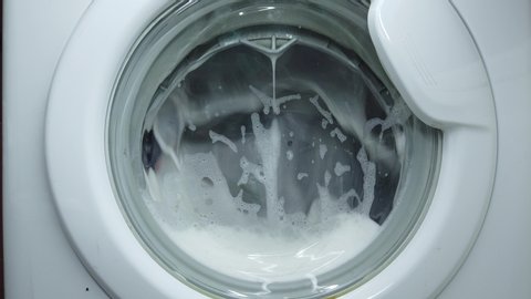 White washing machine washes dirty colorful clothes. Washing clothing in domestic washing machine. Close up video of spinning drum washing machine.