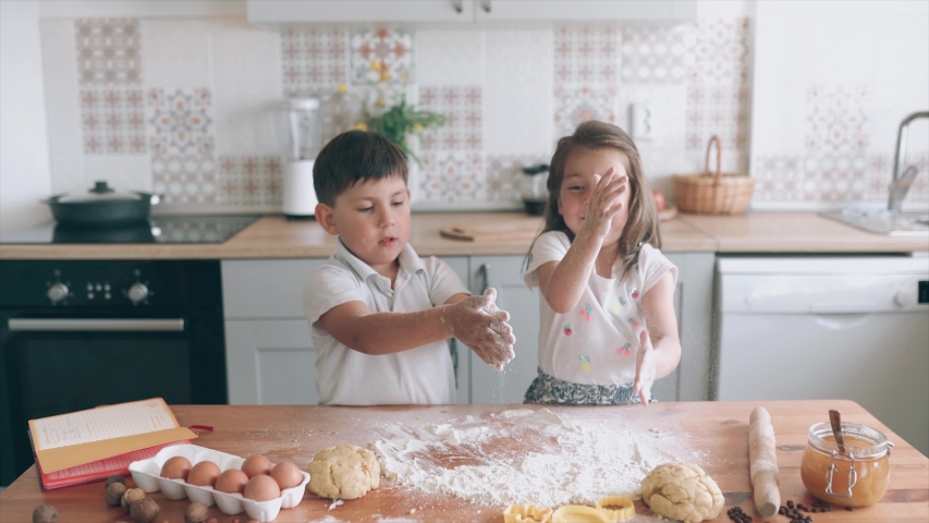 Funny kids cooking together. Girl and boy is beating the dough . Brother and sister in the kitchen. Children are making cakes. Kids have fun. Children study. Homeschooling. Self-isolation. Royalty-Free Stock Footage #1054391429