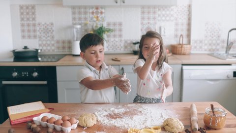 Funny kids cooking together. Girl and boy is beating the dough . Brother and sister in the kitchen. Children are making cakes. Kids have fun. Children study. Homeschooling. Self-isolation.