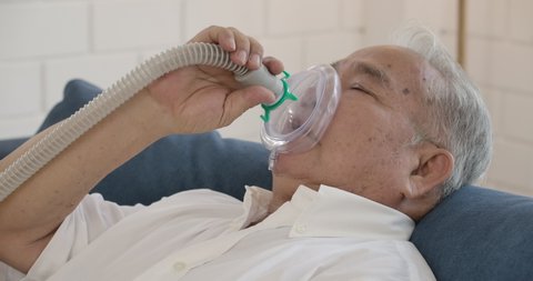 Asian senior elderly man does medical therapy steam inhalation at home. Theme of a serious and incurable disease of lungs and respiratory system. Grandfather breathes in a special medical mask.