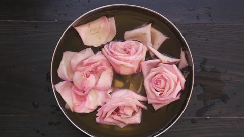 top view female hands using hand skin care bath , bowl with pink roses and rose oil for skin and nails care