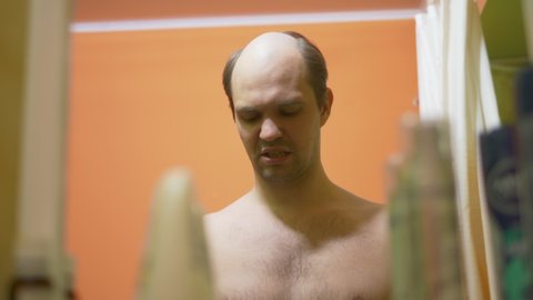 hair loss problem. balding young man looks in the mirror in the bathroom and combes the remaining hair