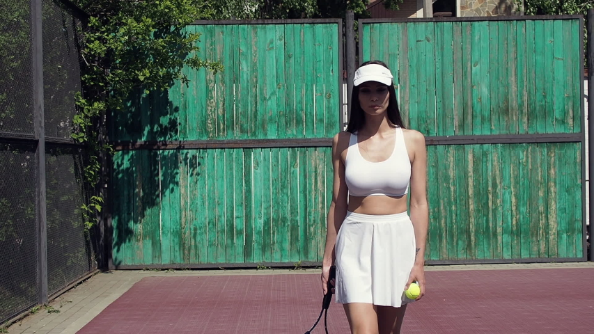 Crop female athlete in white bra and skirt and with racket shifting weight from one leg to another during tennis match on sunny day on court