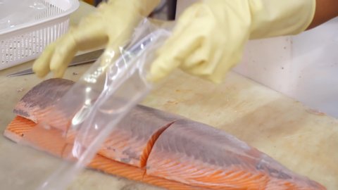 Grocery Store Worker in Rubber Gloves Packs Fresh Salmon Fillets Into Plastic Portion Bags. Packing Fresh Fish for Transportation