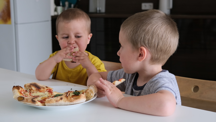 Two mixed age kids eating homemade pizza at home. Two boys enjoy eating pizza with great appetite. | Shutterstock HD Video #1054399613