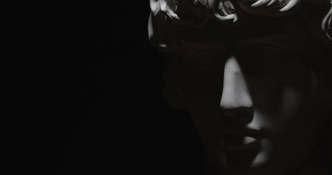 Epic studio close up detail shot. Rotating Antinous gypsum head with moving and changing lighting. The play of light and shadow on half face of statue of man. On black background isolated 4k
