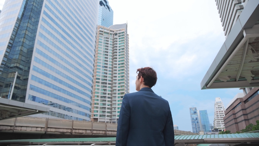 Back view of the Thoughtful Businessman wearing a Suit looking out while standing near modern Office Building background. 4K Slow Motion Corporate. Royalty-Free Stock Footage #1054402961