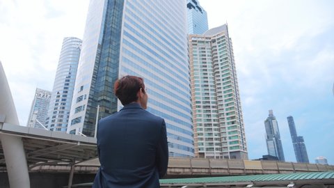 Back view of the Thoughtful Businessman wearing a Suit looking out while standing near modern Office Building background. 4K Slow Motion Corporate.