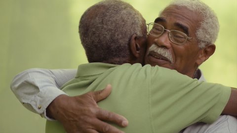 Retired old men and leisure, happy senior black brothers talking and hugging in park. Elderly African american friends embracing, smiling, speaking. Emotional reunion of veterans